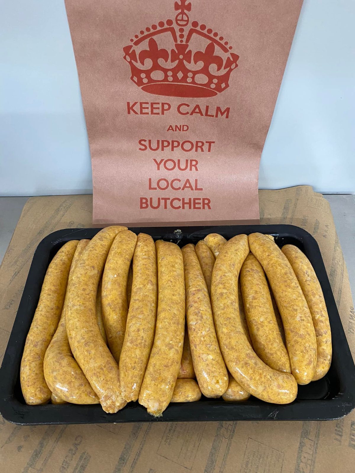A tray of house-made sausages beside a 'Keep calm and support your local butcher' sign